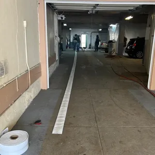 A flat liner rolled out the length of a subterranean parking garage drive aisle, a coil of unused liner in the foreground and the crew set up at the far end